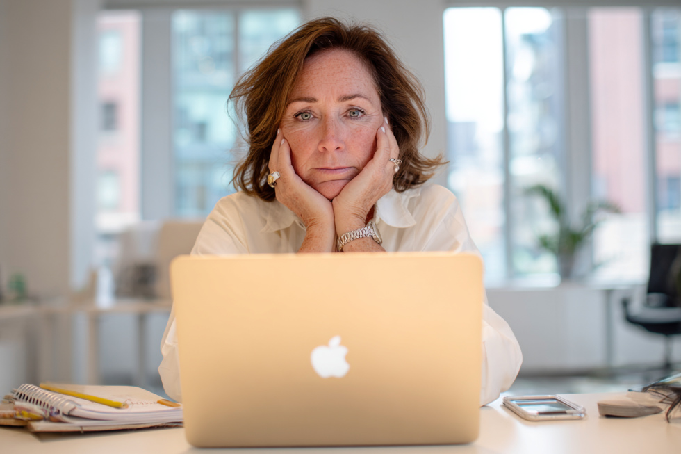 Mittlere europäische Frau im modernen Büro vor MacBook Pro, wirkt gestresst wegen Social-Media-Content-Strategie